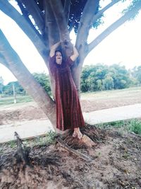 Woman standing by tree trunk on field