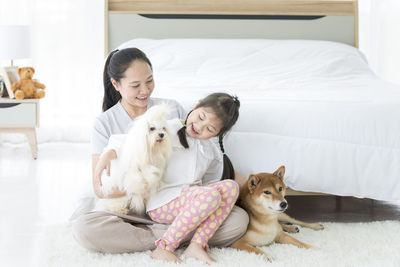 Cheerful mother with daughter and dog sitting by bed