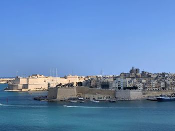 Buildings by sea against clear blue sky