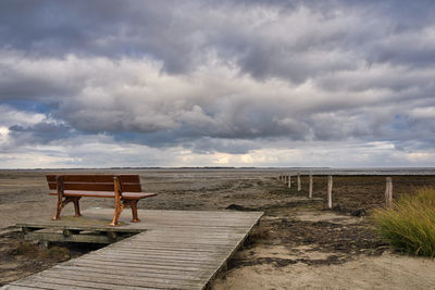 Empty bench on beach against sky