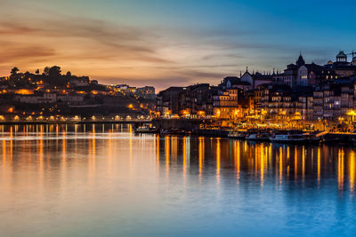 Illuminated city at waterfront during sunset