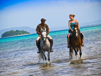 Men riding horse in sea against sky