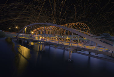 Illuminated bridge over river against sky at night