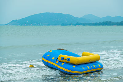 Yellow boat floating on sea against mountains