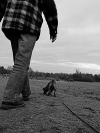 Low section of man with dog standing against sky