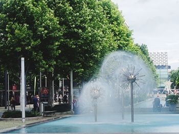 People by fountain in city against sky