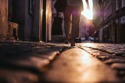 Low section of woman walking on street amidst buildings during sunset