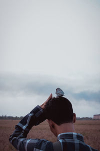 Rear view of man with bird perching on hair against sky