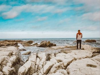 Rear view of man standing on rock at beach against sky