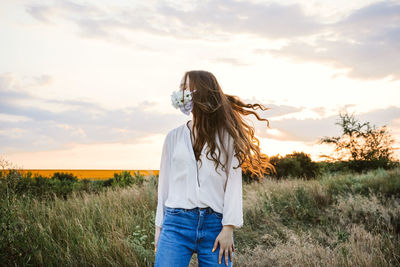 Woman standing on field against sky during sunset