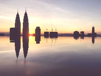 Silhouette buildings by lake against sky during sunset