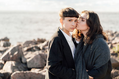 Lesbian women kissing while standing on rock against sea and sky