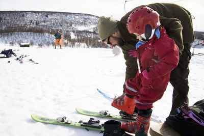 Father helping daughter put on skis