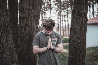 Young man praying by trees on field