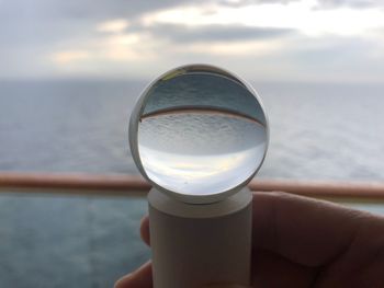 Close-up of hand holding glass against sea