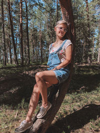 Portrait of smiling young woman sitting on tree trunk in forest