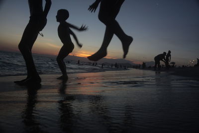 Silhouette people at beach against sky during sunset