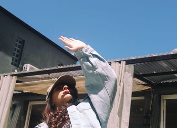 Low angle view of girl gesturing while standing against clear blue sky