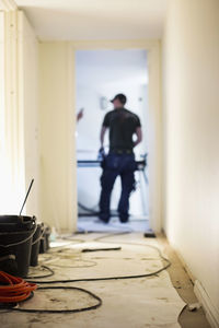 Rear view of carpenter standing at doorway in house under construction