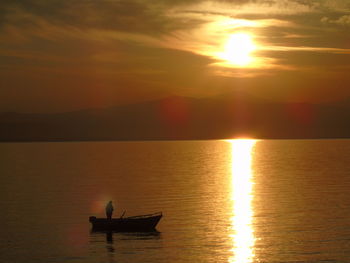 Silhouette man in sea against sky during sunset