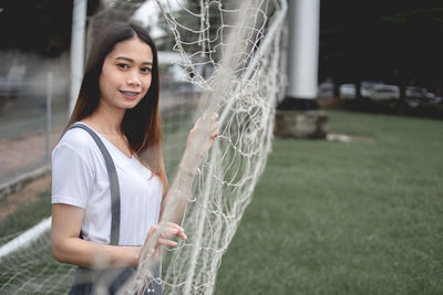 Portrait of smiling young woman standing by net