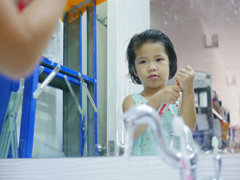 Smiling girl holding toothpaste while standing against mirror 