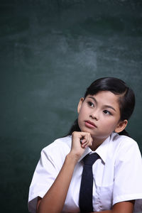 Schoolgirl thinking while studying at table against blackboard