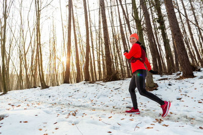 Smiling female runner wearing running vest jogging in forest on cold winter day.