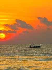 Silhouette man in sea against orange sky