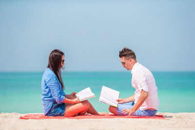 Couple reading books while sitting on beach