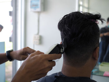 Cropped hands of barber cutting male customer hair in shop