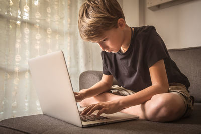 Boy using laptop while sitting on sofa at home