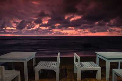 Chairs and table at beach against sky during sunset