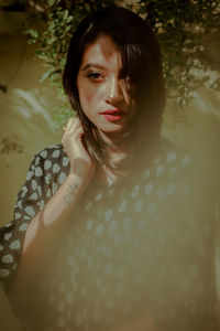 Portrait of beautiful young woman with black hair standing against plants