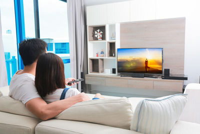 Rear view of couple watching television while sitting on sofa at home