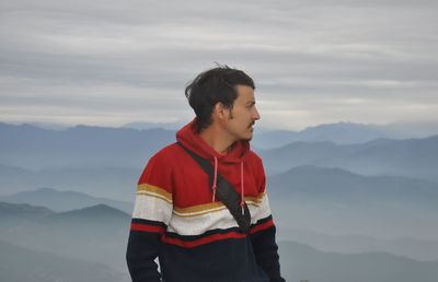 A indian young guy looking sideways while standing against the background of mountains 