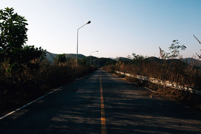 Empty road along trees and plants against sky