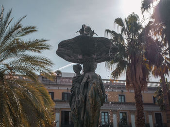 Low angle view of statue by building against sky