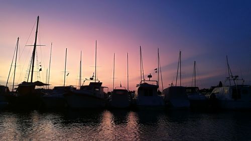 Sailboats moored on harbor against clear sky during sunset