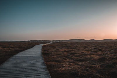 Footpath by sea against sky during sunset