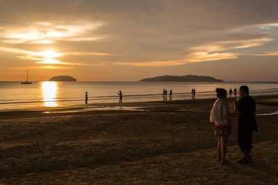 People at beach against sky during sunset