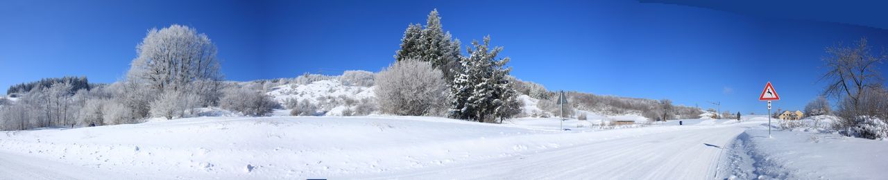 Panoramic view of empty road amidst snowcapped field during winter