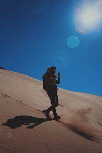 Full length of man walking on sand dune in desert during sunny day