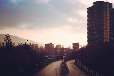 Road amidst buildings against sky during sunset
