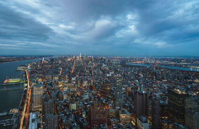 Aerial view of illuminated city against cloudy sky