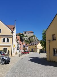 Cars on road by buildings against clear blue sky