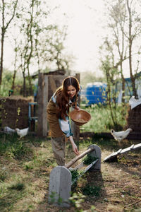 Portrait of young woman feeding chickens at farm