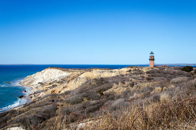 Lighthouse by sea against clear blue sky