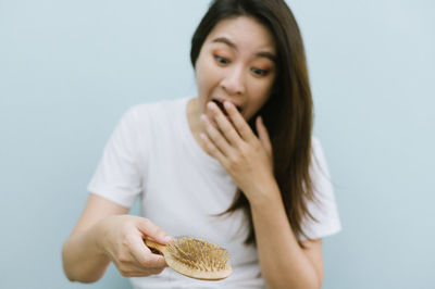 Worried woman holding brush with hair against blue background