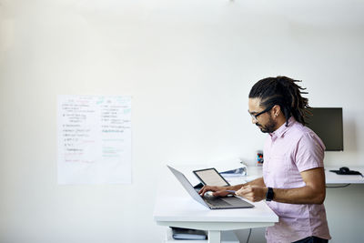 Businessman with credit card doing online shopping over laptop computer on desk against wall in office